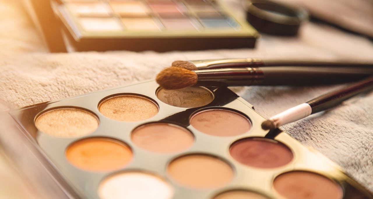 Close-up of a diverse makeup palette with brushes on a textured surface.