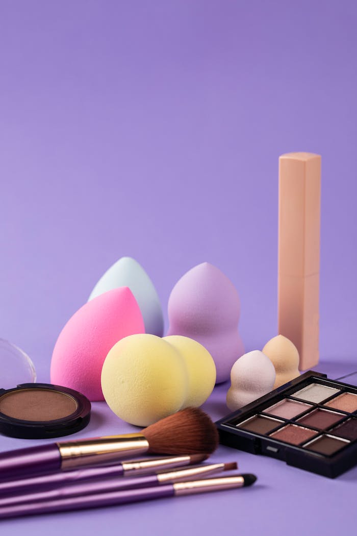 A collection of beauty blenders and makeup products on a purple background.